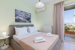Ein Schlafzimmer mit Bett, Nachttisch, Lampe, einem Gemälde und einer Klimaanlage, mit Blick ins Freie.