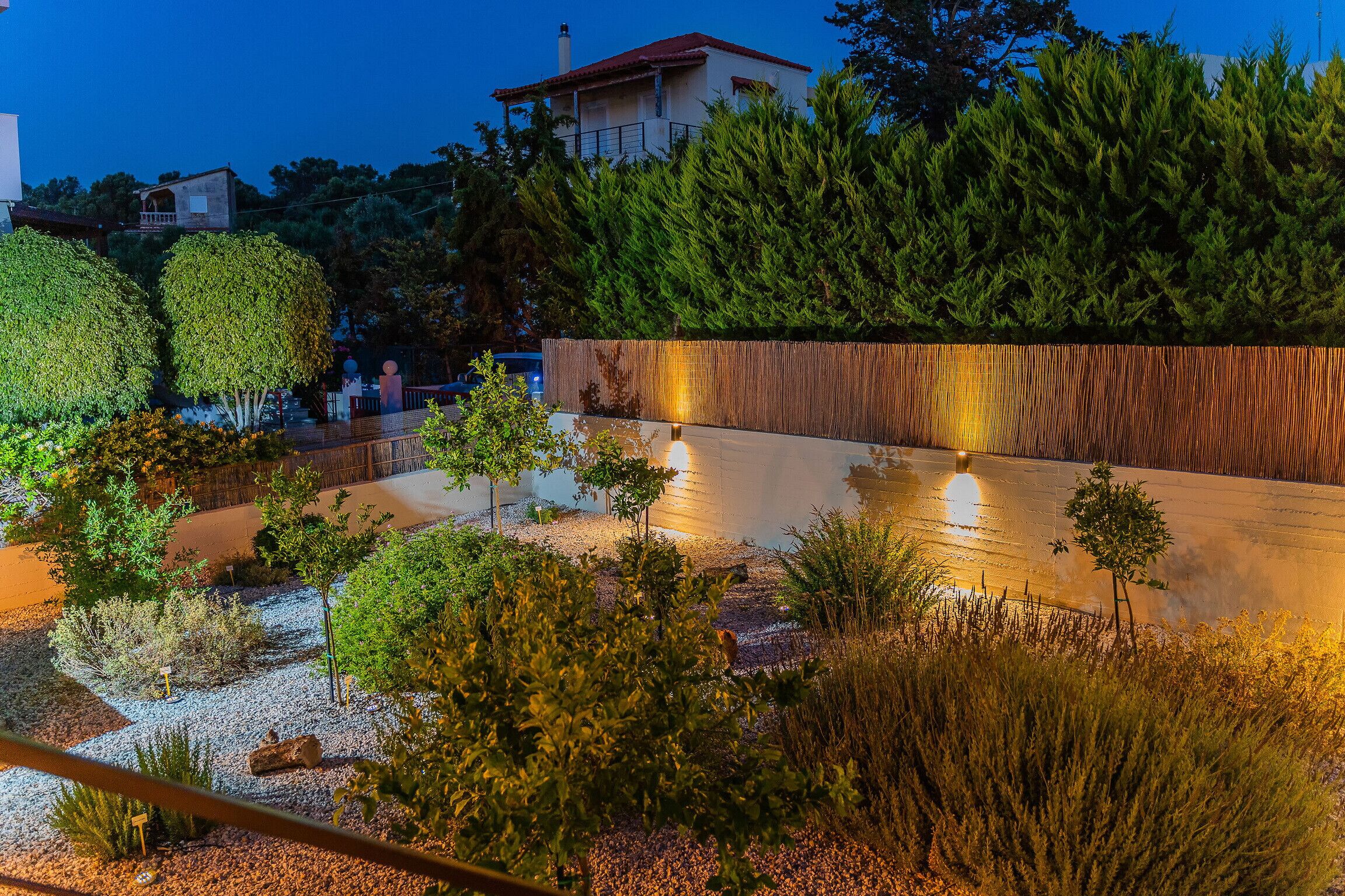 A landscaped garden with a water feature, a wooden wall, and a building in the background.