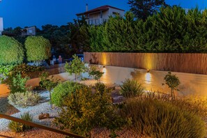 A landscaped garden with a water feature, a wooden wall, and a building in the background. - Papida Grande Villa (Rethymno)