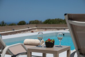 Un ambiente junto a la piscina con dos sillas de descanso, una mesa con una copa de vino blanco y un bol de fresas, y vista al océano.