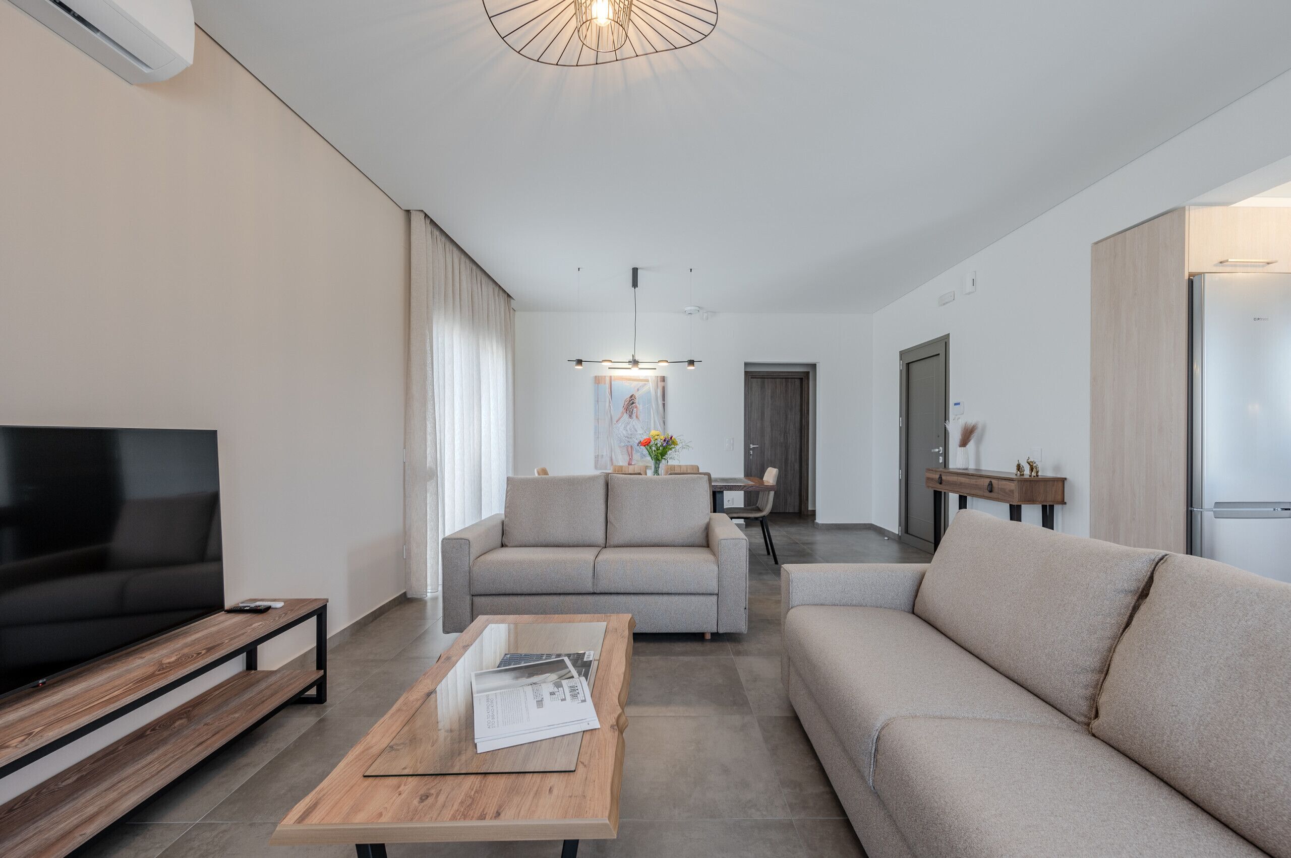 Un salon moderne doté d’un téléviseur à écran plat, d’une table basse en bois, d’un canapé beige et d’un coin repas avec une table et des chaises.