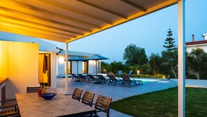 Un patio al aire libre con mesa y sillas, piscina y sillones de descanso.