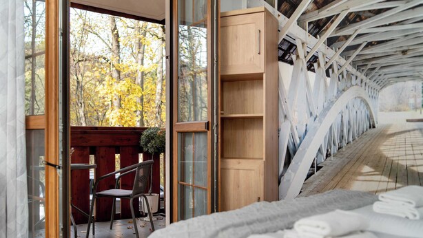 Ein Zimmer mit einem Bett, einem Holzschrank und einer Glastür zu einem Außenbereich mit Sitzgelegenheiten und einem Tisch.