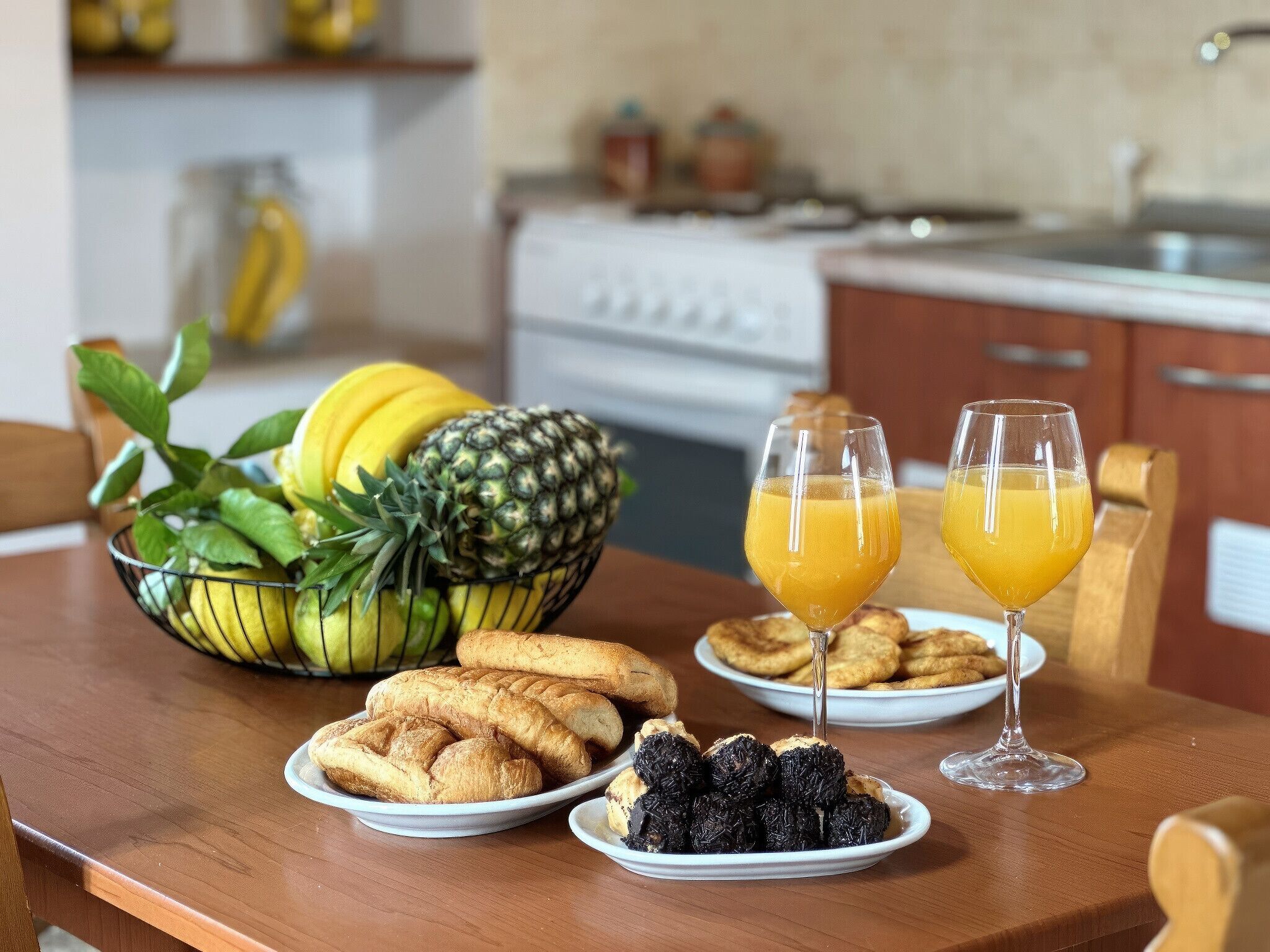 A breakfast table with fruits, pastries, and orange juice glasses.