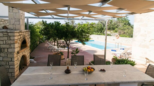 Un área de comedor exterior con chimenea de piedra, piscina y vistas al área de la piscina.