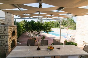 Un espace extérieur aménagé pour les repas, avec une cheminée en pierre, une piscine et une vue sur l’ensemble de l’espace piscine.