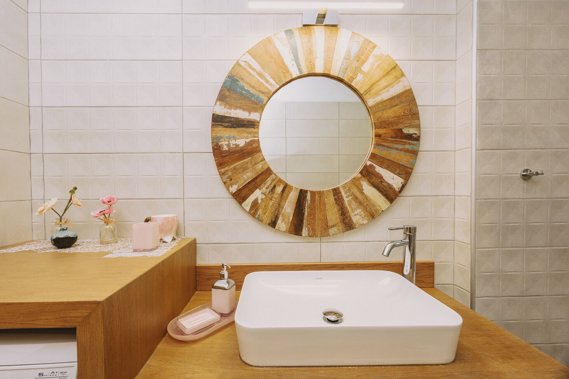 Un baño con un espejo redondo, un lavamanos blanco y un mueble de tocador de madera.