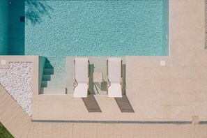 En vy från ovan av en swimmingpool med två solstolar och en kant av småsten.