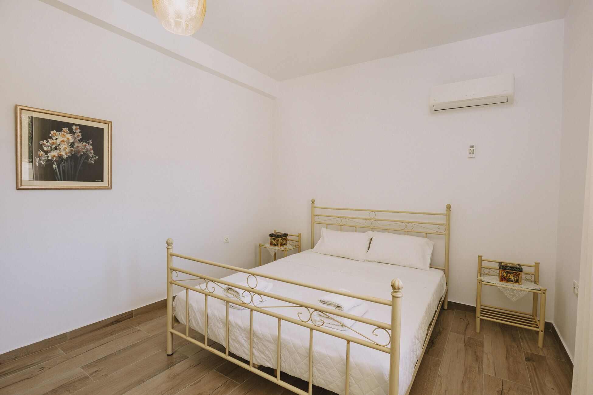 Une chambre avec un lit simple, une table de chevet, une commode, un appareil de climatisation et un tableau encadré au mur.