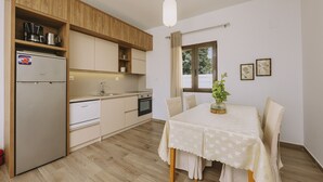 A compact kitchen with wooden cabinets, a built-in oven, and a dining area with a table and chairs. - Villa Panormo Crete (Mylopotamos)