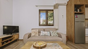 A living room with a sofa, a TV, a wooden coffee table with candles, and a view of the outdoors through a window. - Villa Panormo Crete (Mylopotamos)
