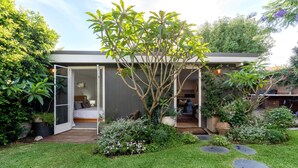 A modern house with a covered outdoor seating area, a visible bedroom, and a garden with various plants and a small tree. - Tranquil & Spacious Parkside Retreat in Willoughby (Willoughby East)