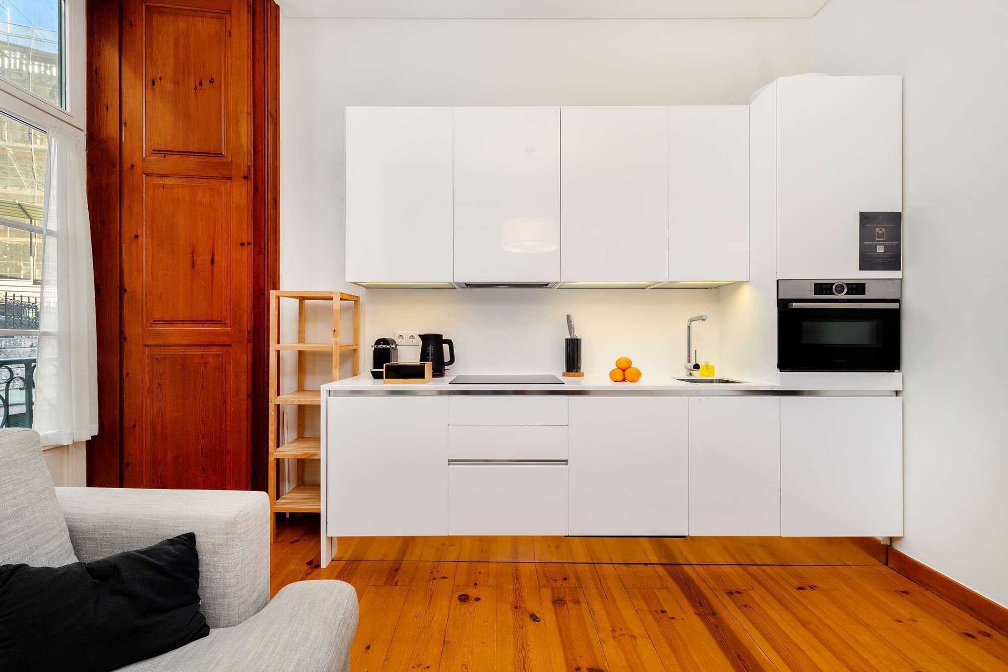 Una cocina moderna con armarios blancos, horno empotrado y cafetera.