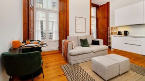 A modern living room with a sofa, ottoman, and a dining area with a table set for breakfast. - Modern Comfort in Old Lisbon (Lisbon)