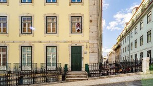 A yellow building with a green door and windows, a stone facade, and a wrought iron fence. - Modern Comfort in Old Lisbon (Lisbon)