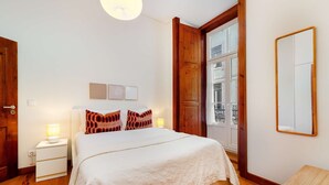 A bedroom with a bed, bedside tables, a wooden wardrobe, a mirror, and a window with a view of the street. - Modern Comfort in Old Lisbon (Lisbon)