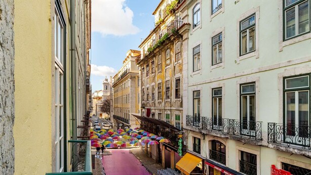 A narrow street with colorful umbrellas, a pink pathway, and buildings with balconies and signage. - Modern Comfort in Old Lisbon (Lisbon)