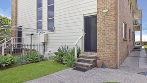 A two-story building with a brick section and a white siding section. There is a front door with a small porch and steps leading up to it. - Upper Oceanside (AVOCA BEACH)