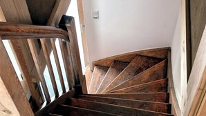 Una escalera de madera con barandilla que conduce a un rellano con pared blanca y un interruptor de luz.