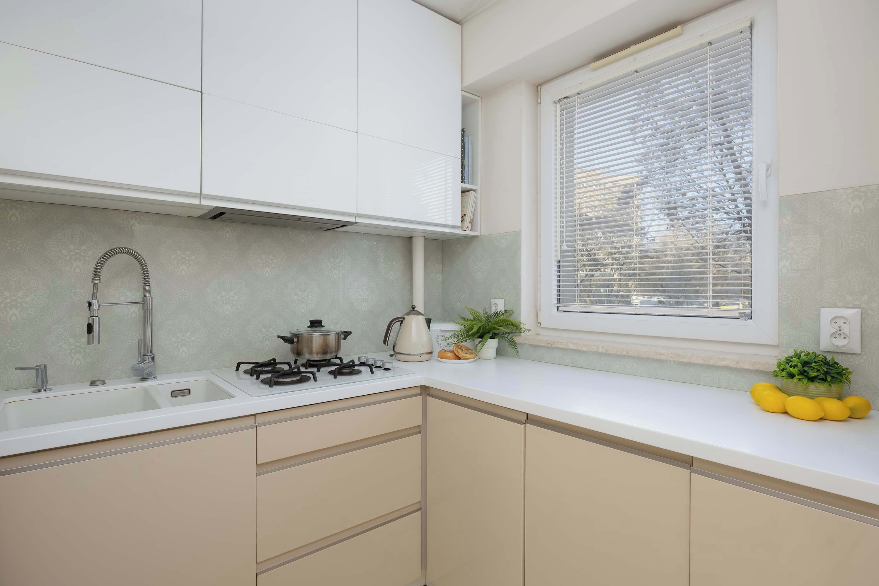 A kitchen with white cabinets, a sink, a stove, and a window with blinds.