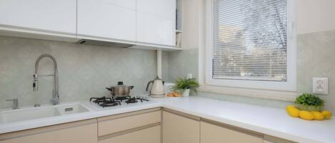 A kitchen with white cabinets, a sink, a stove, and a window with blinds.