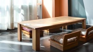 A modern living room with a wooden table and two sofas, a large window with curtains, and a unique wall design. - Pie My Love (Vientiane)