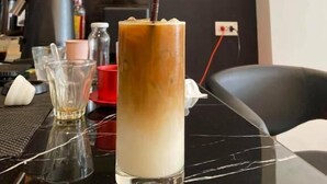 A menu board with drink options and prices, a coffee grinder, a glass of iced coffee with a straw, and a coffee cup on a table. - Pie My Love (Vientiane)