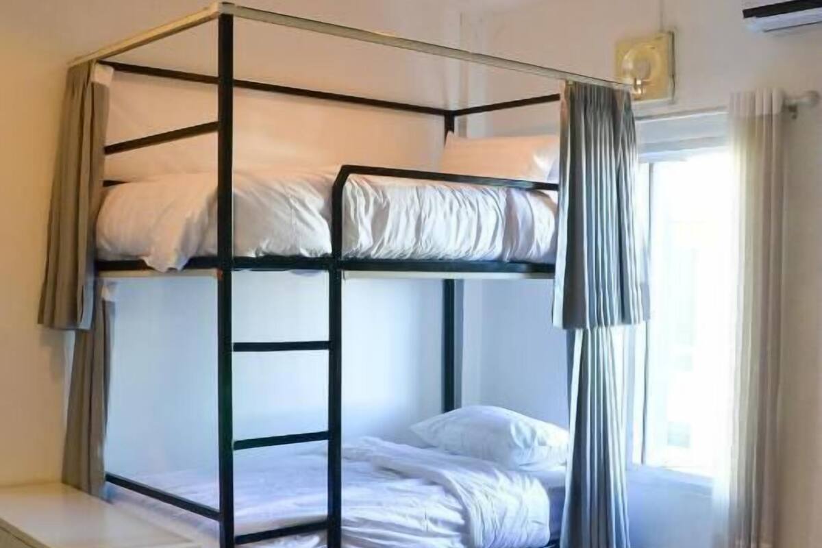 Habitación con literas, un escritorio blanco, una ventana con cortinas y un equipo de aire acondicionado.