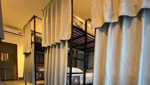 A row of bunk beds with white curtains, wooden flooring, and a door in the background. - Pie My Love (Vientiane)