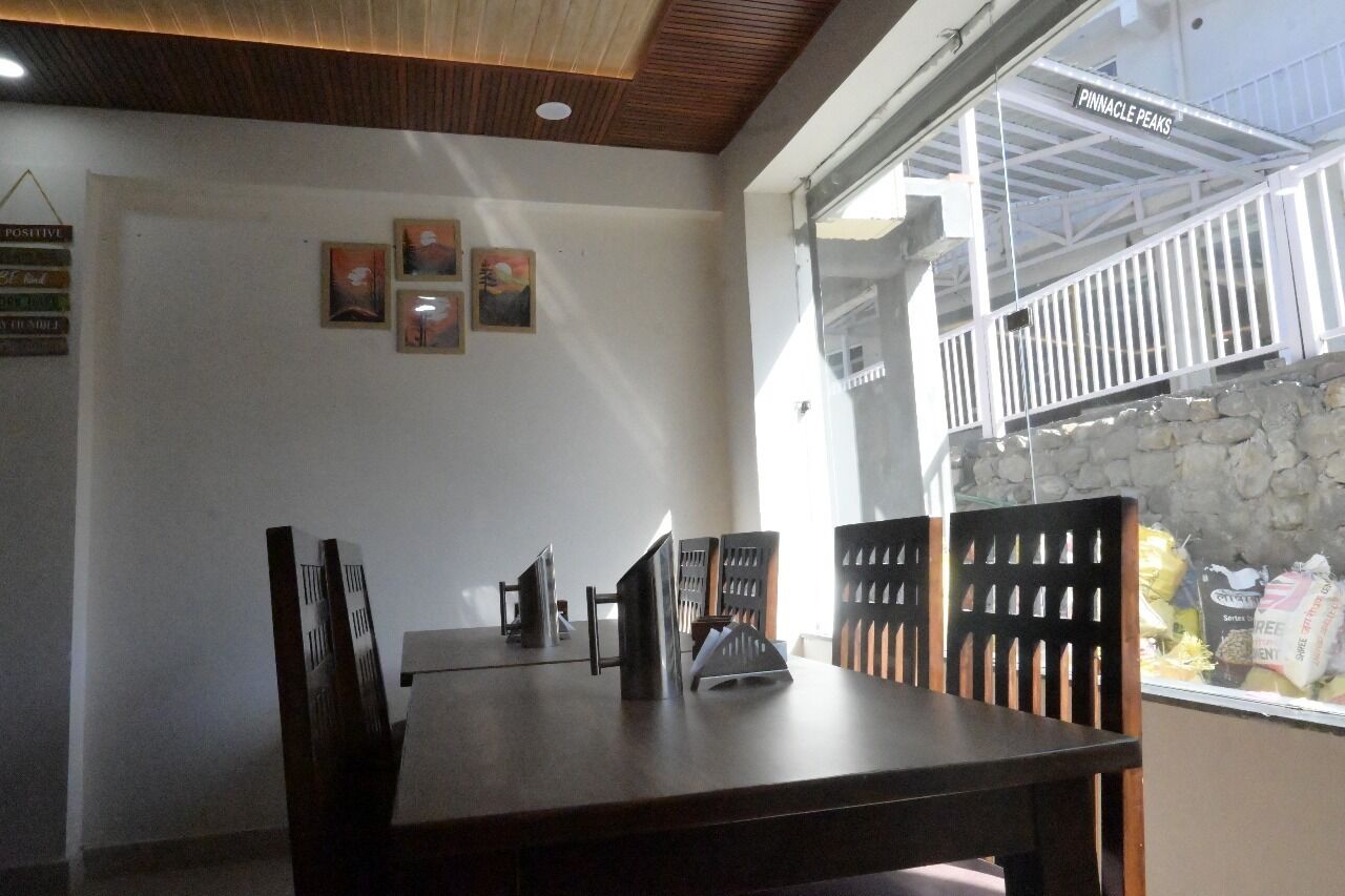 A dining area with a wooden table and chairs, framed pictures on the wall, and a view of a balcony with a railing.