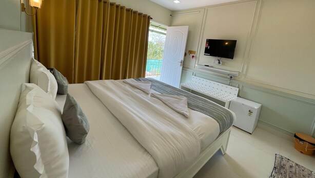 Una habitación de hotel con cama, televisión, ventilador de techo y ventana con cortinas.