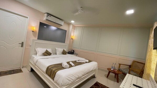 A hotel room with a bed, bedside table, chair, and an air conditioning unit.