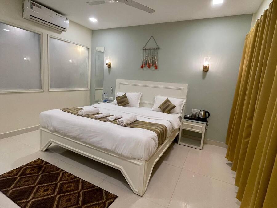 Habitación de hotel con cama, mesita de noche, equipo de aire acondicionado y ventana con cortinas.