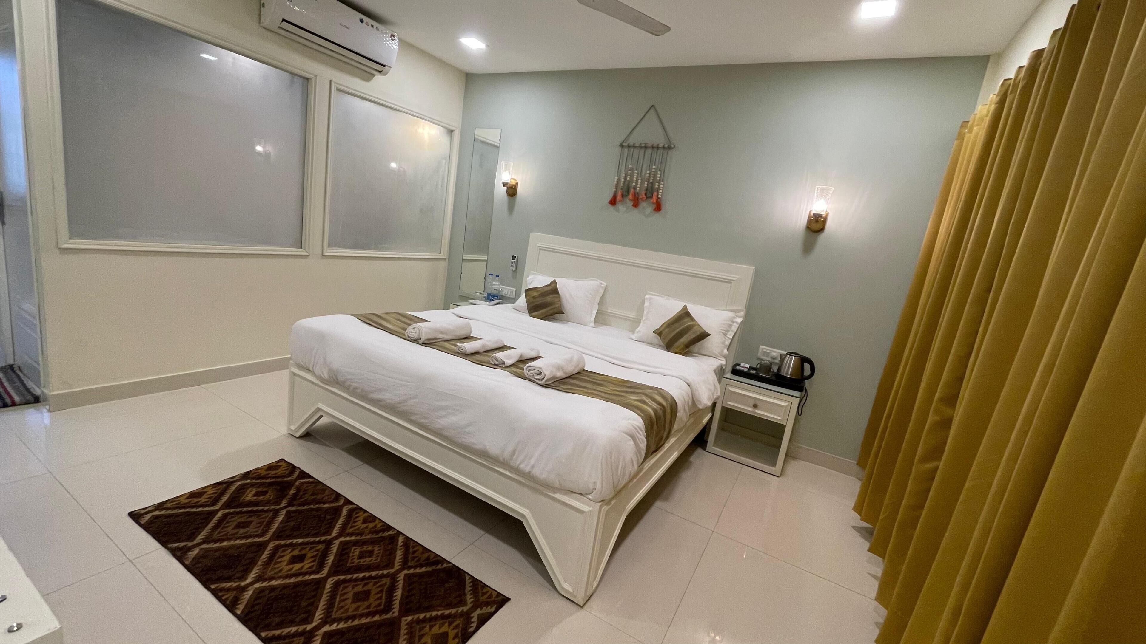 A hotel room with a large bed, bedside tables, a wall-mounted air conditioner, and a patterned rug.