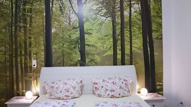 Ein Schlafzimmer mit einem Bett, zwei Nachttischen und einer Wandmalerei zum Thema Wald.
