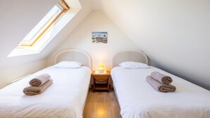 Une chambre avec deux lits, une lucarne, une petite table avec une lampe et un tableau au mur.