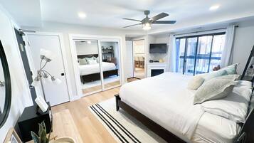 Un dormitorio moderno con una cama grande, ventilador de techo, televisor y puerta corredera hacia un baño.
