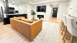 A modern living room with a sofa, a dining area with chairs, a kitchen with a TV, and a fireplace. - Ski-In/Out Luxury / Central Location / King, Chef’s Kitchen / Park City Mtn Base (Park City)