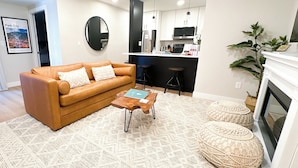 A modern living room with a brown leather sofa, a coffee table, and a patterned rug. There is a kitchen area with a microwave and a sink. - Ski-In/Out Luxury / Central Location / King, Chef’s Kitchen / Park City Mtn Base (Park City)