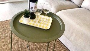 Ein Wohnzimmer mit einer Couch, einem grünen Tablett mit einer Flasche und Gläsern sowie einer Topfpflanze.