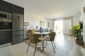 Een moderne keuken met inbouwapparatuur, een eethoek met rieten stoelen, en uitzicht op de woonkamer.