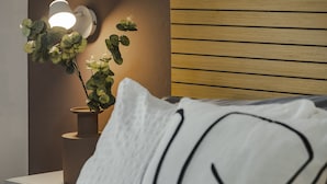 Ein Bett mit weißem Kissen, ein Nachttisch mit Topfpflanze und eine Wandleuchte.