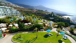Ein Resort mit Poolbereich, Liegestühlen und Blick auf das Meer und die Berge.