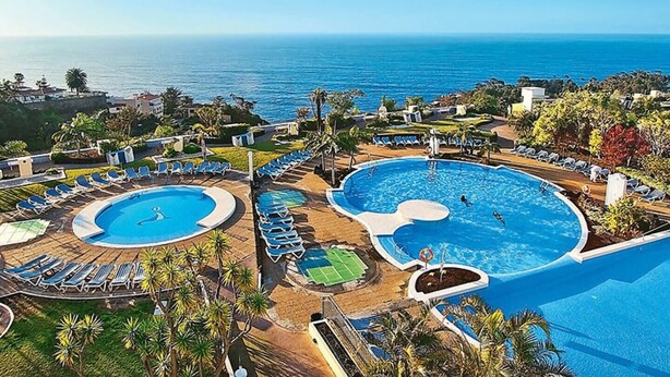 Ein Resort mit zwei großen Schwimmbecken, Liegestühlen und Blick auf den Ozean.