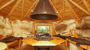 A rustic wooden interior with a central wood-burning stove, fur-covered walls, and a view through a doorway. - Quietly situated vacation apartment - Ferienhaus Weingarten FeWo zum Fischer (Ostseebad Baabe)