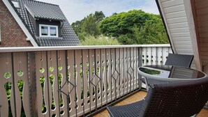 A balcony with a glass table and chairs, a view of a house with a sloped roof, and a green hedge in the background. - Quietly situated vacation apartment - Ferienhaus Weingarten FeWo zum Fischer (Ostseebad Baabe)