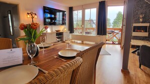 Un comedor con una mesa de madera dispuesta para dos personas, un jarrón con tulipanes y un menú. Un televisor de pantalla plana está montado en la pared sobre la mesa.