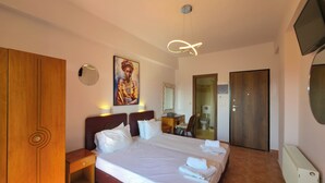 A hotel room with a large bed, a wooden wardrobe, a painting on the wall, a bathroom with a toilet and sink, and a TV mounted on the wall. - Welcome to Double Room – Olympic Studios by SDR (Paralia)