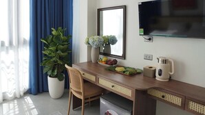 Ett modernt hotellrum med ett skrivbord i trä, en stor krukväxt, en platt-TV och en inbyggd luftkonditioneringsanläggning.