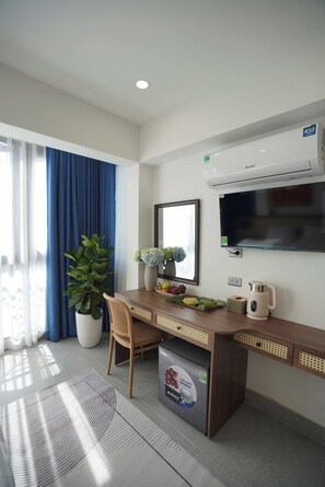 Ein modernes Hotelzimmer mit Schreibtisch aus Holz, einer großen Kübelpflanze, einem Flachbildfernseher und einer eingebauten Klimaanlage.
